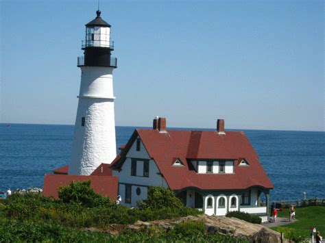 A White And Red House Next To The Ocean With A Light House On Its Roof