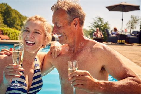 retired senior couple relaxing in swimming pool on summer vacation celebrating drinking