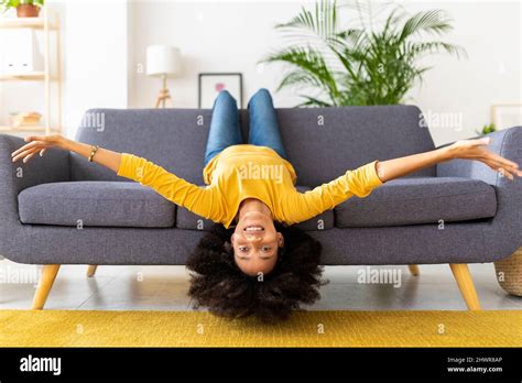 Happy Young Woman Lying Upside Down On Sofa In Living Room At Home