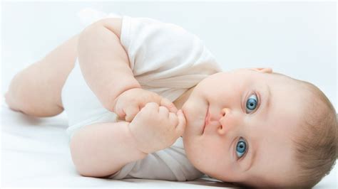 Cute Blue Eyes Baby Is Lying Down On Floor Wearing White