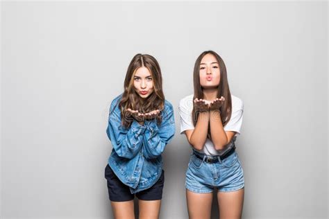 Portrait Of Two Beautiful Young Girls Blowing Kisses To Camera Isolated On The Gray Background