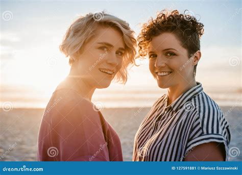 Smiling Lesbian Couple Standing Together On A Beach At Sunset Stock Image Image Of Lesbian