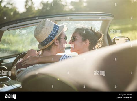 Rear View A Young Trendy Couple Kissing In A Convertible Car On A