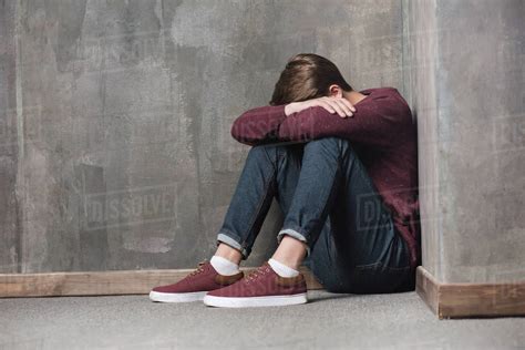 Depressed Teenage Boy Sitting On Floor With Head In Hands Stock Photo