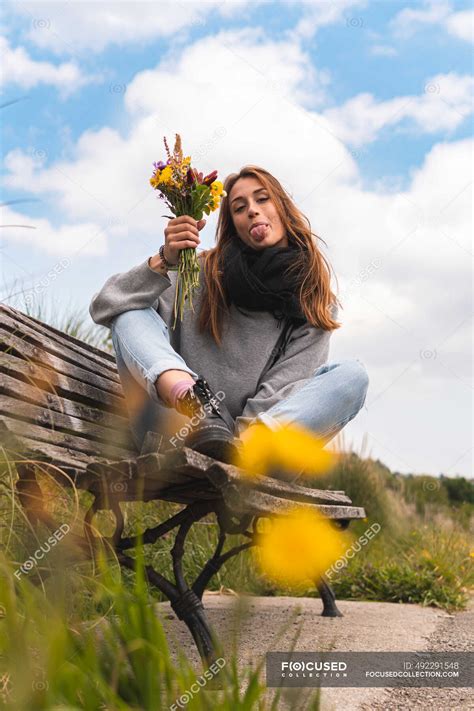 Young Woman Sticking Out Tongue While Sitting With Bunch Of Flowers On Bench — Adults Lifestyle
