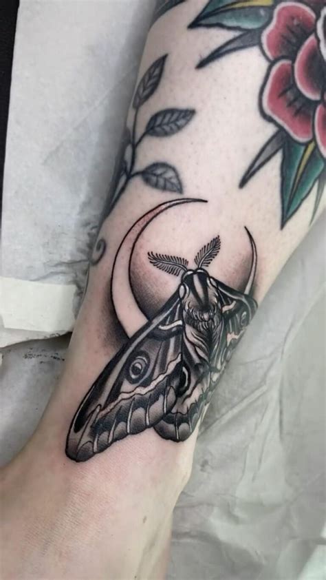A Black And White Photo Of A Moth On The Arm With Flowers Around It