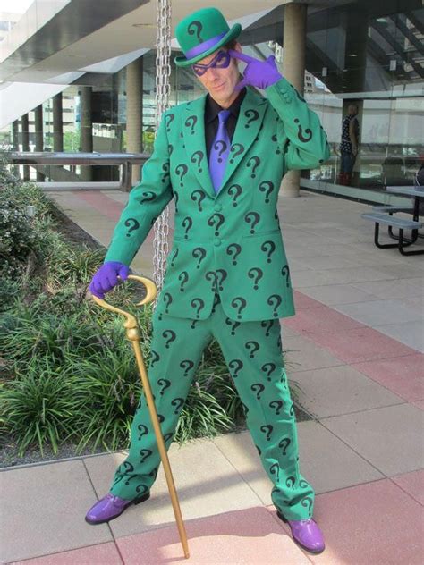 a man in a green suit and top hat holding a cane with question marks on it