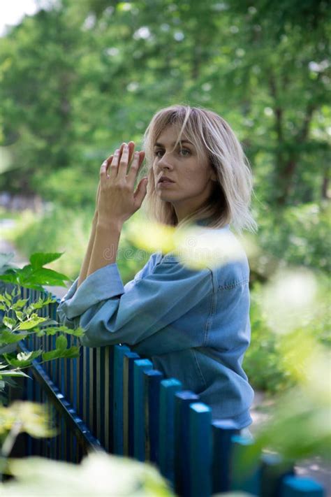 Girl With Blond Hair And A Blue Denim Jacket Is Leaning Against A Blue Fence Stock Image Image