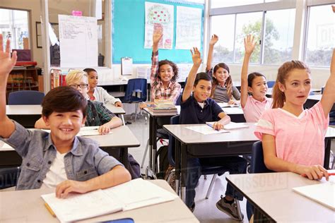 Elementary School Kids In A Classroom Raising Their Hands Stock Photo