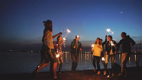 Group Of Young Friends Having A Beach Party Friends Dancing And Celebrating With Sparklers In