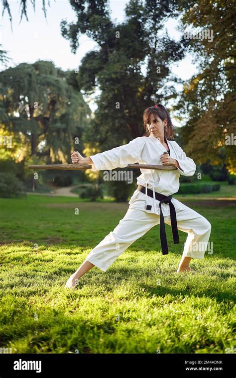 female karate fighter in white kimono and black belt practicing karate outdoors in the nature