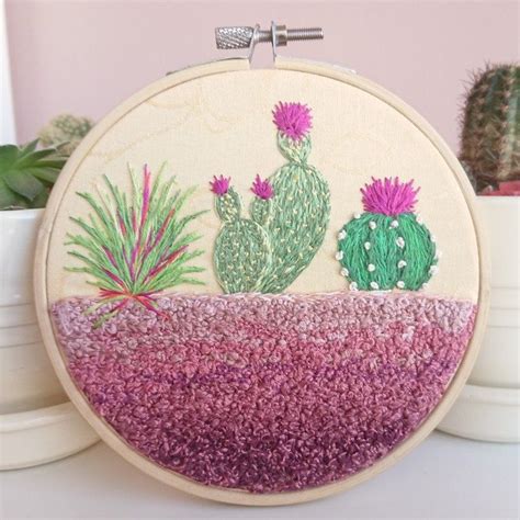A Hand Embroidered Hoop Hanging On A Wall Next To Some Potted Plants And Cacti