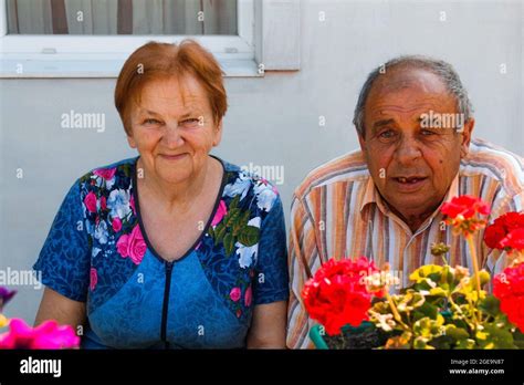 Elderly Couple Smiling In Summer Day Happy Elderly Pair Of Husband And Wife Seating On Flowers