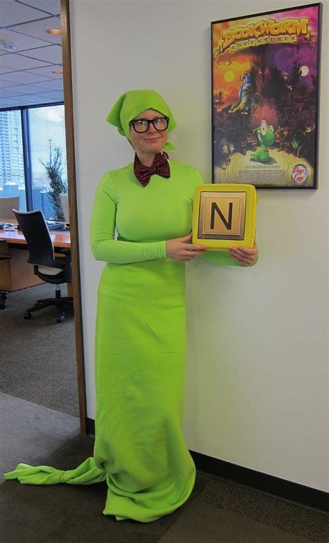 A Woman In A Green Dress And Bow Tie Holding Up A Wooden Block With The Letter N On It