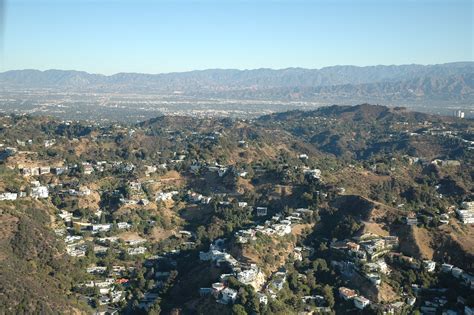 An Aerial View Of A City With Mountains In The Back Ground And Trees To