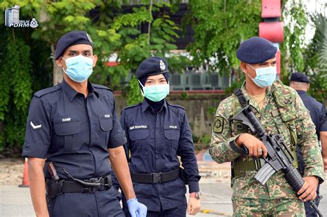 royal malaysian police officer aided by soldiers manning the roadblock during movement control