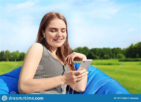 Young Woman Listening To Music While Sitting On Bean Bag Chair Outdoors