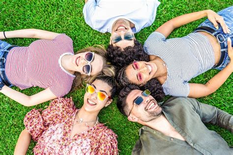 Group Of Friends Lying On Park Meadow Wearing Colored Trendy Sunglasses