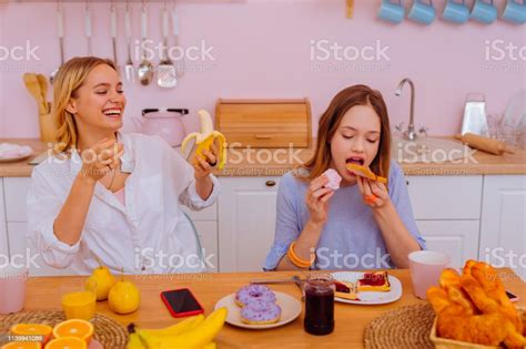 Sister Laughing Watching Teenage Sibling Eating Too Much Sweets Stock