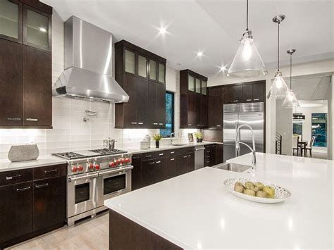 Light gray kitchen cabinets boast a white quartz countertop holding a gas integrated cooktop beneath a light gray wood range hood flanked by stacked gray shaker cabinets mounted against white and gray marble chevron backsplash tiles. 53 High-End Contemporary Kitchen Designs (With Natural ...