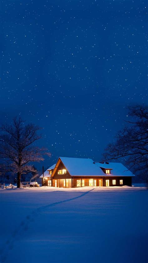A House Is Lit Up At Night In The Snow With Stars Above It And Trees