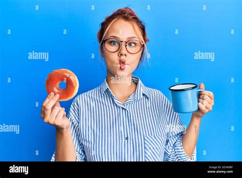 Joven Mujer Pelirroja Comiendo El Desayuno Sosteniendo Donut De Chocolate Y Café Haciendo Cara