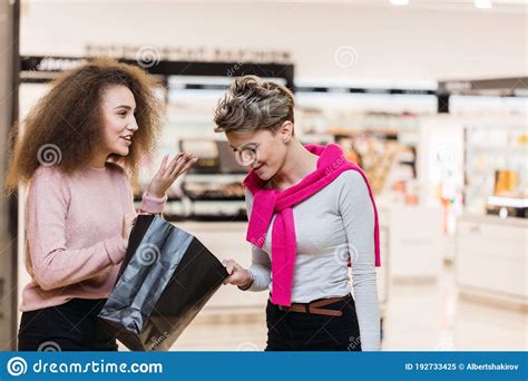 Brunette And Blonde Looking At Shopping Bag To Each Other Discussing Purchases Stock Image