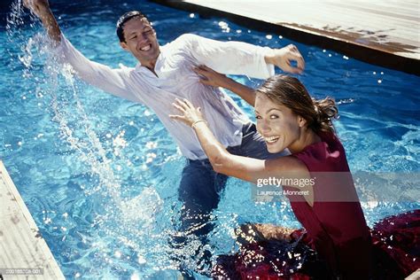 Couple In Swimming Pool With Clothes On Having Water Fight High Res