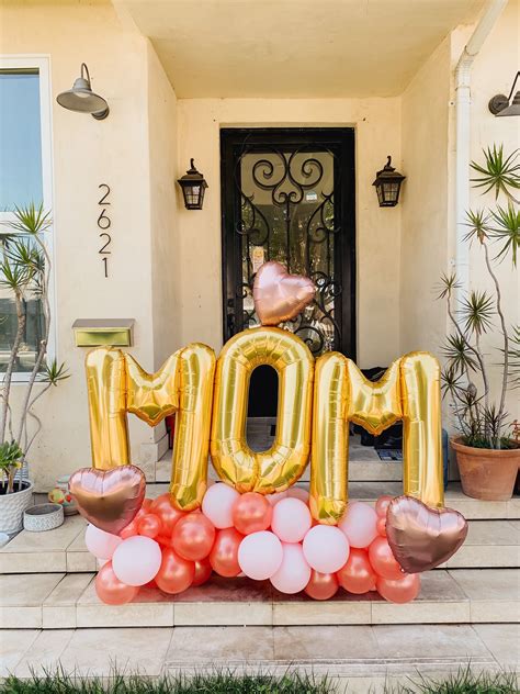 A Large Balloon That Says Mom In Front Of A House With Pink And Gold Balloons