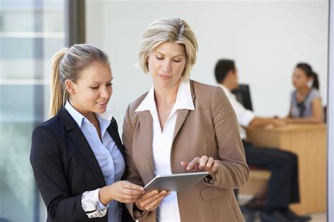 Two Female Executives Looking At Tablet Computer With Office Meeting In
