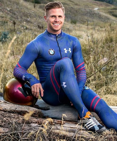 A Man Sitting On Top Of A Log Wearing A Wet Suit And Holding A Helmet