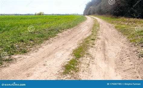 Empty Single Lane Dirt Road In Countryside Running Between Green Meadow