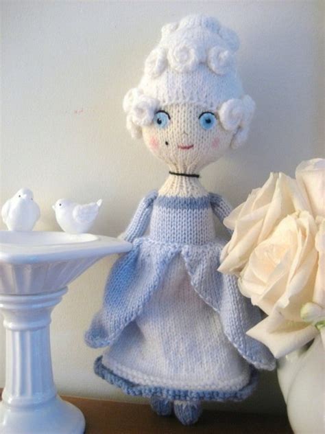 A Knitted Doll Sitting Next To A White Flower Vase