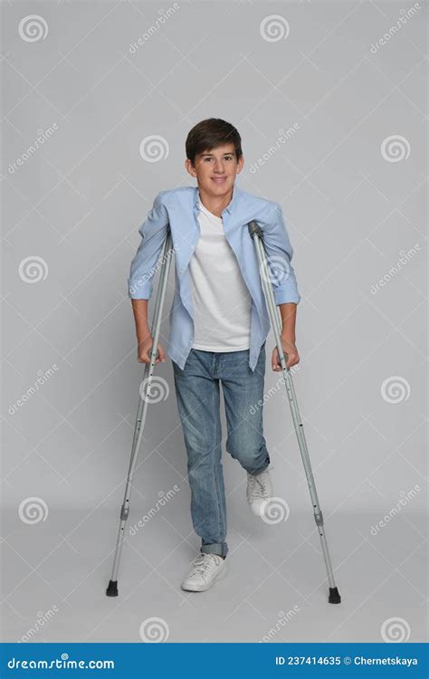 Teenage Boy With Injured Leg Using Crutches On Grey Background Stock