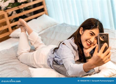 Happy Young Woman Taking Selfie Photo With Her Mobile Phone While Lying Down In Bedroom At Home