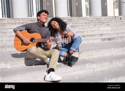 A Young Latin Couple In Love Playing The Guitar And Singing Sitting On