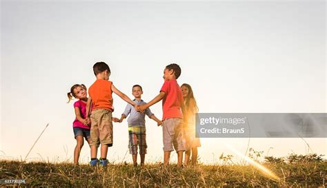 Below View Of Cute Friends Playing Ringaroundtherosy At Sunset High Res