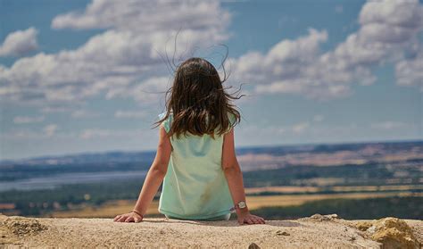 Girl Sitting On Her Back In Landscape And Blue Sky With White Clouds