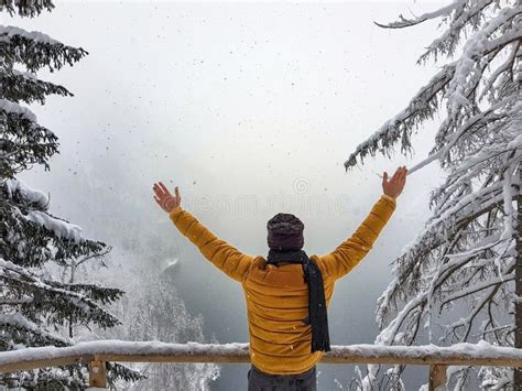Man Dressed In Warm Clothes With His Hands In The Air Near Snowy Trees