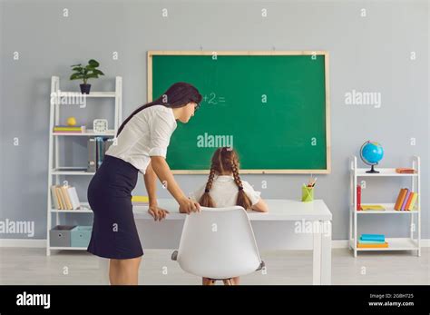 Female Teacher Helping Little Girl On Math Lesson At Classroom Tutor