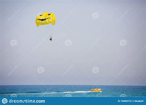 Couple Of Tourists Flying On A Yellow Parachute With Smiling Face On It