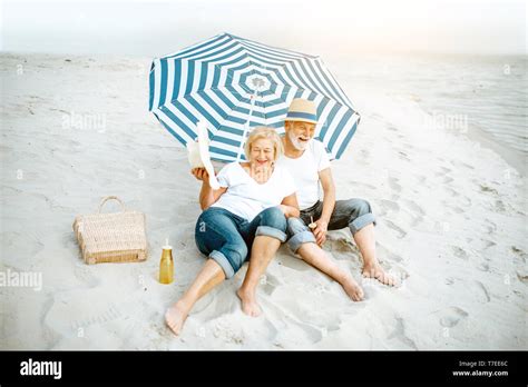 Happy Senior Couple Relaxing Lying Together Under Umbrella On The Sandy Beach Enjoying Their