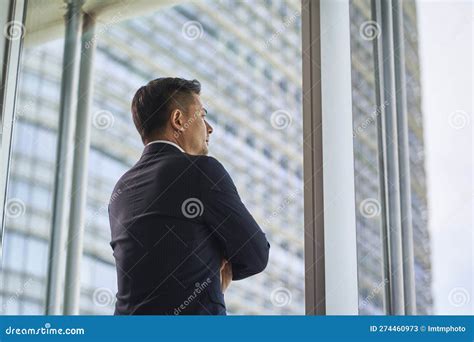 Asian Businessman Standing By Window Looking At View Stock Image