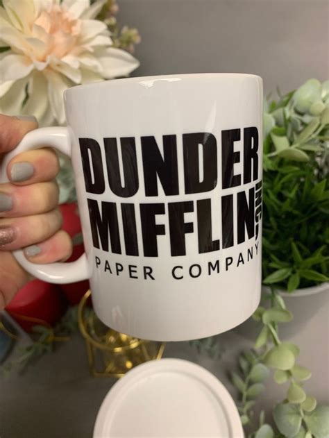 A White Coffee Mug With The Words Dunder Mifflin Paper Company On It