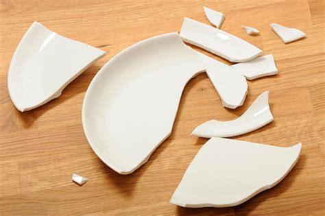A Broken White Ceramic Plate On A Wooden Floor Stock Photo Download