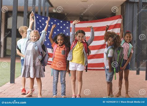 Happy School Students Standing In Corridor While Holding American Flag