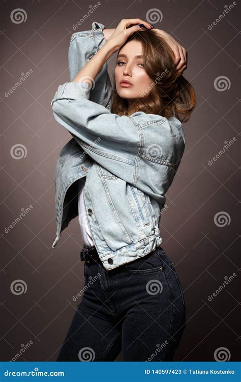 Beautiful Brunette Girl With Long Flowing Hair Dressed In Jeans Jacket And Jeans Poses Holding