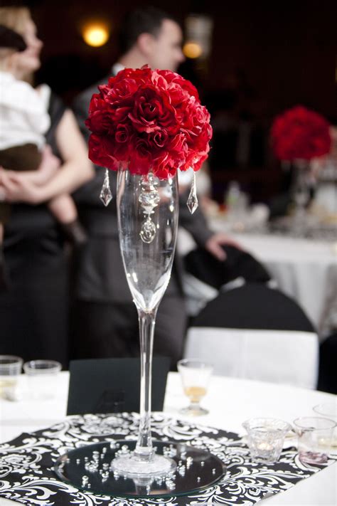 A Tall Glass Vase Filled With Red Flowers On Top Of A White Tablecloth