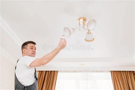 A Male Electrician Changes The Light Bulbs In The Ceiling Light Stock