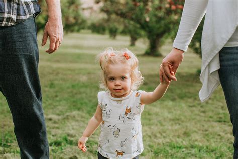 Little Girl Walking With Parents And Holding Moms Hand By Stocksy